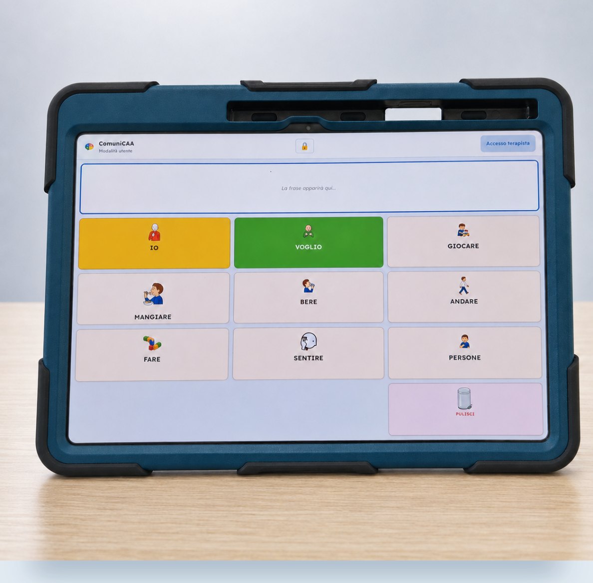 Tablet ComuniCAA nella custodia protettiva blu, appoggiato su un tavolo: barra della frase e griglia di simboli IO, VOGLIO, GIOCARE, MANGIARE, BERE, ANDARE.